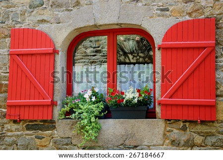 Old stone house with red wooden shutters. Boxes with red and white flowers on the window. Brittany, France