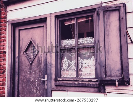 A front of the house. A door and a window with white lace curtain decorated with windmill and tree pattern and wooden hinged shutters . (Amiens, Picardy, France)  Rustic background. Toned photo.