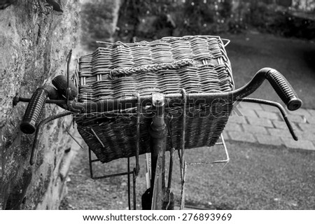 Rusty vintage bicycle with wicker basket leaning on a stone wall. Closeup. Back view. Aged photo. Black and white.