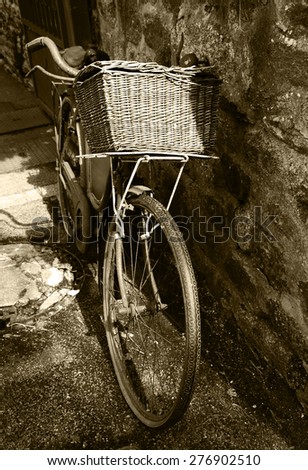 Rusty vintage bicycle with wicker basket leaning on a stone wall. Brittany, France. A game of light and shadow. Aged photo. Sepia.
