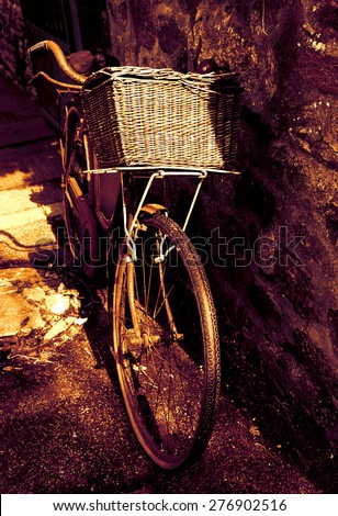 Rusty vintage bicycle with wicker basket leaning on a stone wall. Brittany, France. A game of light and shadow. Toned photo.