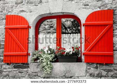 Old stone house with red wooden shutters. Boxes with red and white flowers on the window. Brittany, France. Retro aged photo.