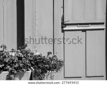A wooden house door and geranium flowers in the boxes in sunny day. Brittany, France. Aged photo. Black and white.