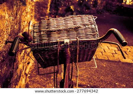 Rusty vintage bicycle with wicker basket leaning on a stone wall. Closeup. Back view. Toned photo.