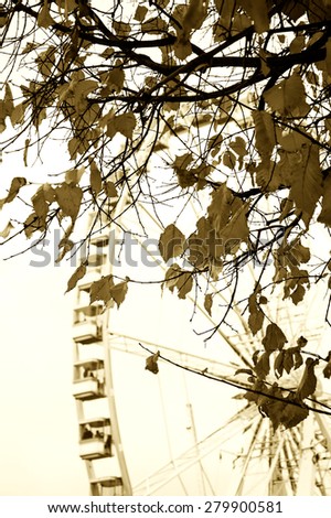 Autumn in Paris. Branches with faded leaves and ferris wheel silhouette at background. Selective focus on the leaves. Aged photo. Sepia.