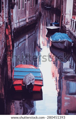 Narrow canal in Venice. Boats and reflection of colorful houses in the water. Selective focus on the  reflection. Retro aged photo.