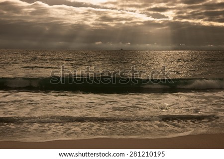 Dramatic cloudy sunset with sunbeams over Atlantic Ocean coast. Fishing ship sailing on horizon under sun rays glowing through the clouds. Nazare, Portugal. Toned photo.