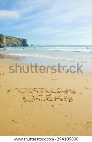Words PORTUGAL and OCEAN are written on the scenic beach in the Algarve region of Portugal. People swimming and surfing.