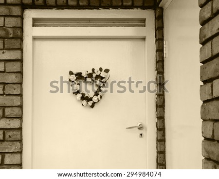Wedding (or birth) flower wreath in heart shape on door. London, UK. Aged photo. Sepia.