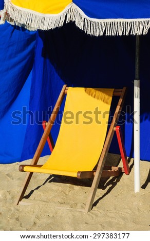 Beach wooden chaise lounge and umbrella with fringe. Trouville-sur-Mer (Normandy, France). Selected focus on the fringe.