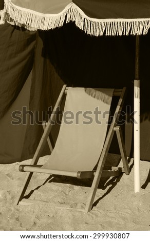 Beach wooden chaise lounge and umbrella with fringe. Trouville-sur-Mer (Normandy, France). Selected focus on the fringe. Aged photo. Sepia.