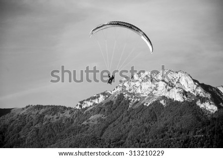 Paragliders flying in tandem and mountains of Savoy at background (Annecy Lake, France) . Aged photo. Black and white.