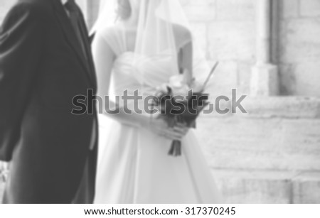 Blurred photo of bride and her father waiting before entering to the Gothic church on wedding day (father is taking his young daughter to the altar). Black and white.
