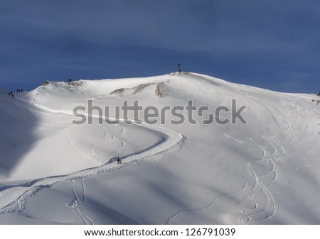 Winding winter hiking path in the distance through snow dunes up to a summit with cross