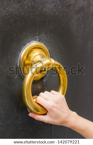 Fair, small female hand holding a golden door knocker ring on a door in Modena, Emilia-Romagna, Italy