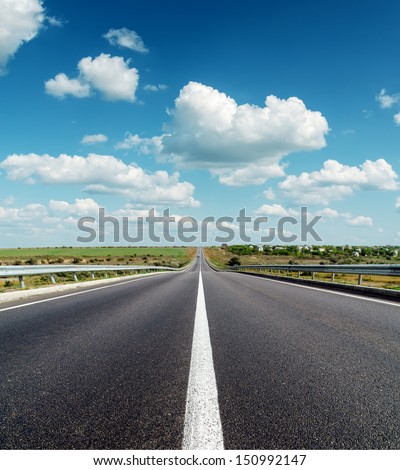 black asphalt road to horizon under deep blue cloudy sky
