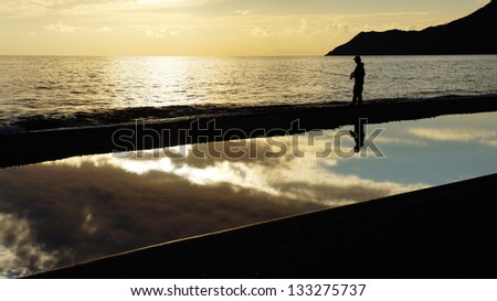 Fisher man with fishing rod silhouette on the beach at sunset