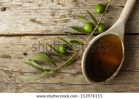 Green olive branch and a spoon full of oil on the wooden table