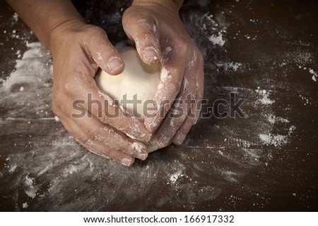 woman\'s hands kneading dough on wooden table