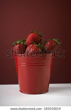 fresh red strawberries in a red bowl on checkered tablecloth, with red background