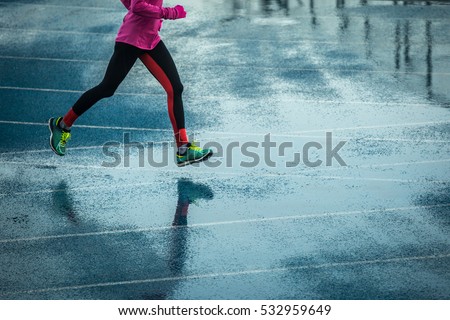 Young woman running on track in rainy weather splashing puddles.