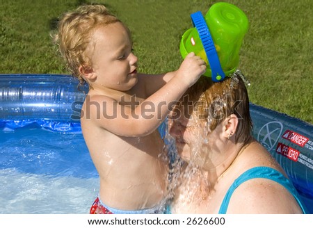 Young boy dumping a bucket of water on a woman in swimming pool