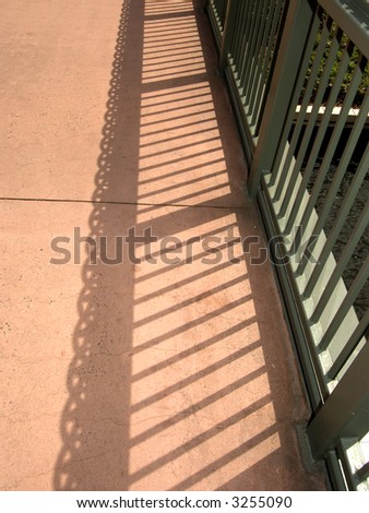 Linear shadows of railing on red sidewalk