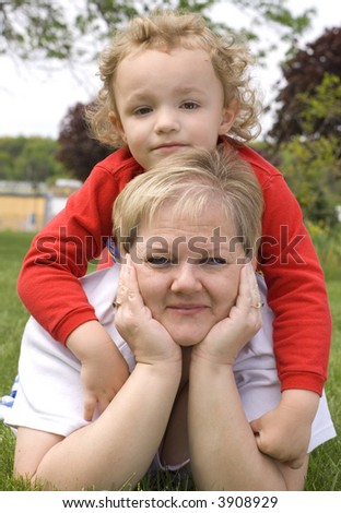 Son laying on top of mother\'s back outside on grass