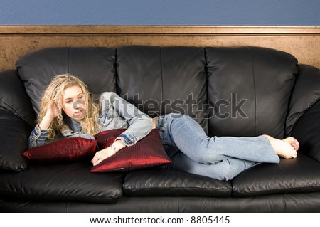 Beautiful blond model relaxing on black leather couch/sofa