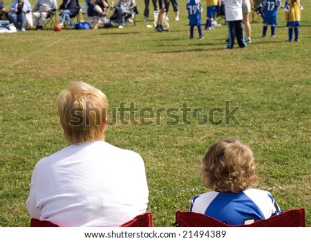 Mother and son watching soccer game from sideline sitting in chairs