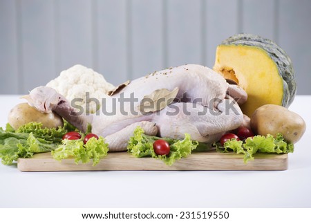 Raw whole chicken on the board with tomato , pumpkin, lettuce and potato
