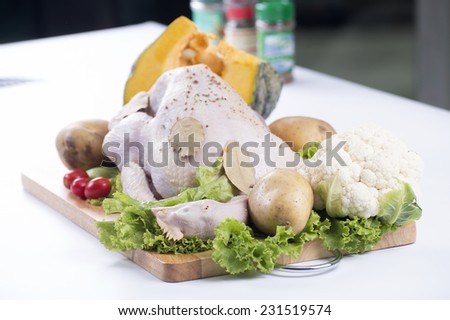 Raw whole chicken on the board with tomato , pumpkin, lettuce and potato