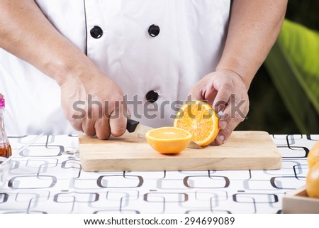 chef cutting orange on old wooden broad with knife
