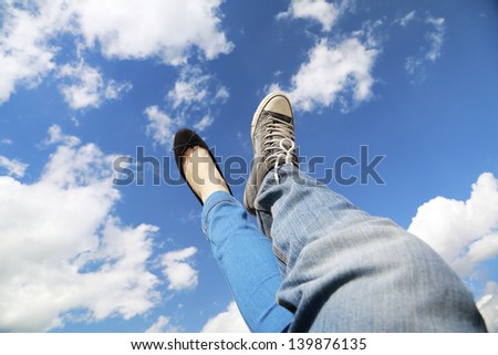 legs dangling in the blue sky with clouds