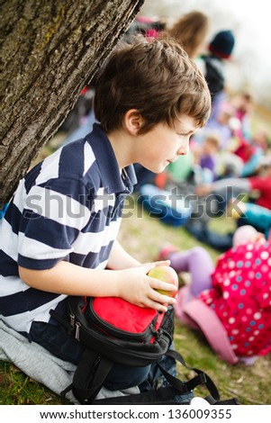 Boy sitting by a tree eating an apple on a school trip