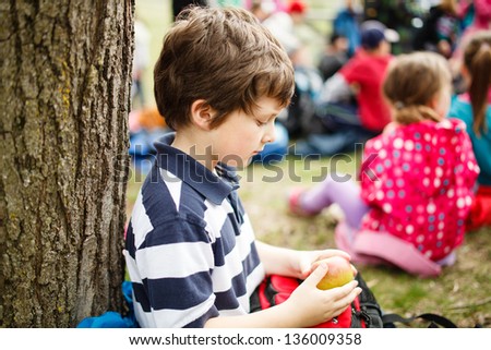 Boy sitting by a tree eating an apple on a school trip