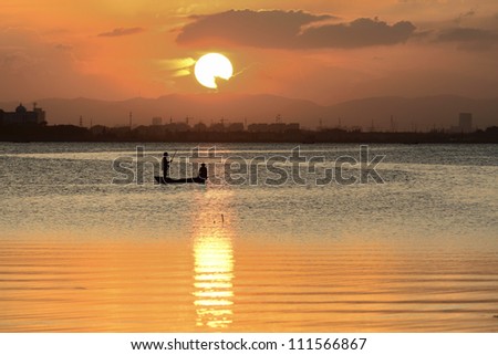 Sunset from a Chinese countryside Lake, two fishermen are working.
