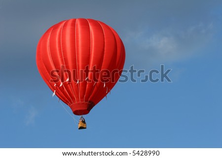a red hot air balloon in a cloudy blue sky