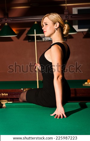beautiful blonde young woman at the billiards is sitting on the table