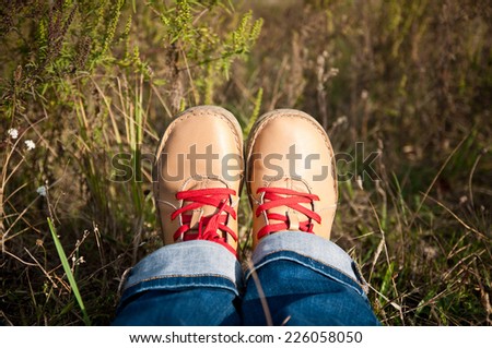nice camel color shoes with red shoelaces and blue jeans at the grass