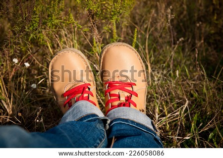 nice camel color shoes with red shoelaces and blue jeans at the grass