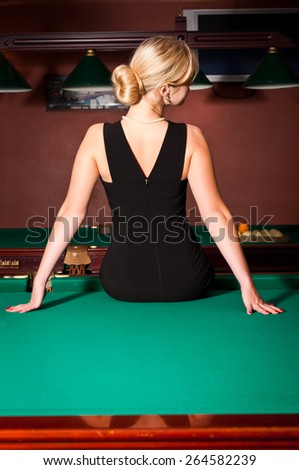 blonde young woman in black strict dress sitting on the billiards table