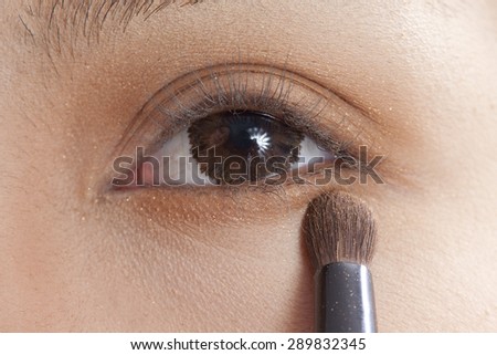 close up portrait of beautiful young brunette woman applying eye-zone make up with cosmetic brush