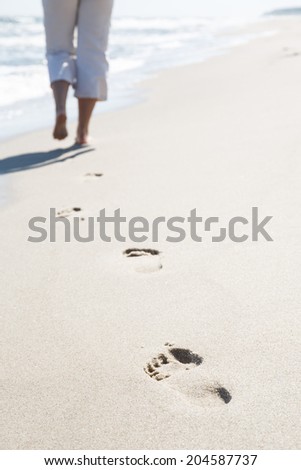 Footprints on the beach. Lonely woman departing into the distance over the sea