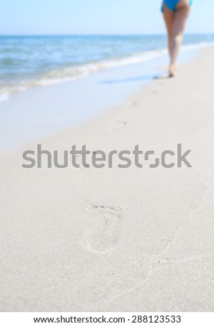Footprints on the beach. Lonely woman departing into the distance over the sea. Small depth of field