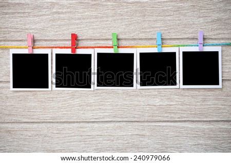 empty black photo frames hanging with clothespins on wooden background