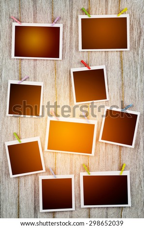 empty black photo frames hanging with clothespins on wooden background in vintage tone