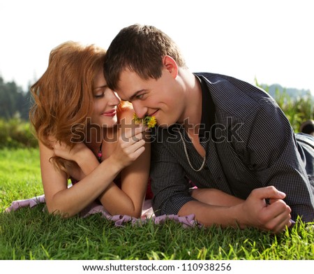 Handsome man and woman lying in the grass holding yellow little flowers