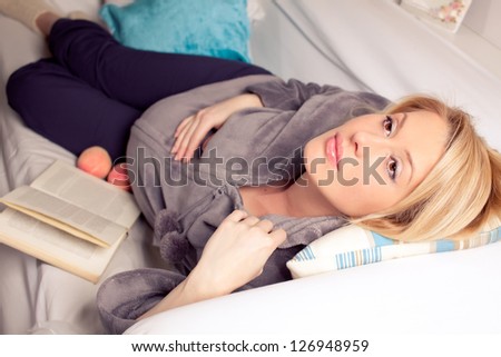 Pregnant blonde woman relaxing on sofa, reading book, dreaming,