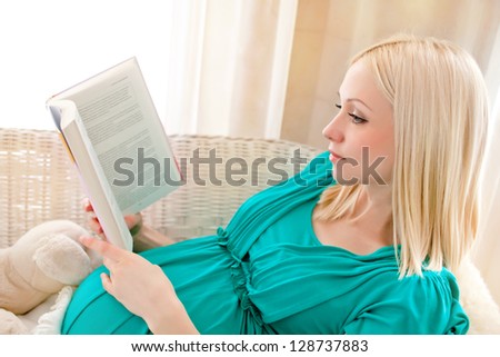 Pregnant blonde woman relaxing on sofa, reading book, dreaming,